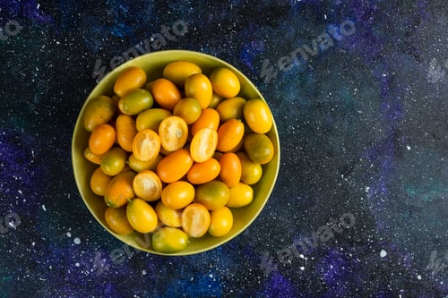 Preview: Top View. Pile of kumquats in ceramic bowl over blue background