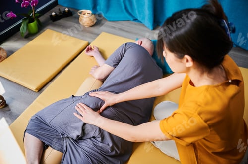 Preview: Masseuse making thai yoga massage. Woman therapist doing traditional massage treatment for patient.