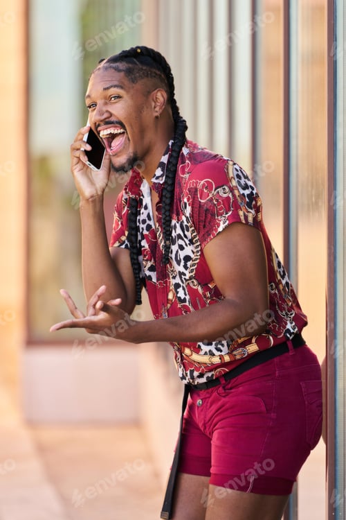 Preview: A gay man with braids talks on his cell phone. He smiles and makes a funny face