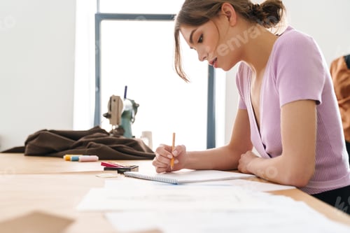 Vorschau: Foto einer Modedesignerin, die während der Arbeit am Tisch Skizzen macht