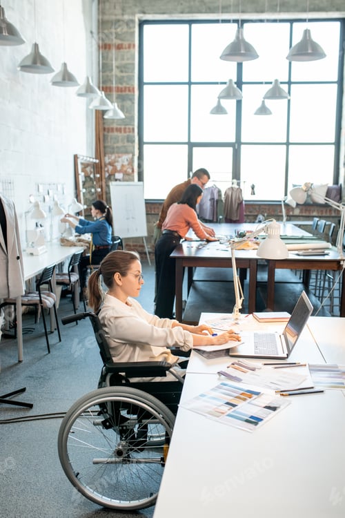 Preview: Young creative designer in wheelchair sitting in front of laptop while looking through online ideas