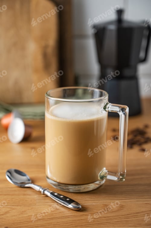 Preview: Cup of freshly brewed aromatic coffee with milk on the kitchen table with a coffee pot