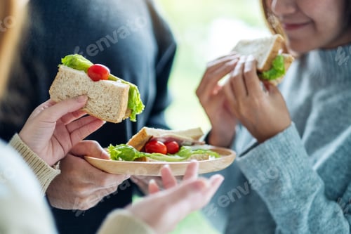 Preview: Group of young people holding and eating whole wheat sandwich in wooden plate together