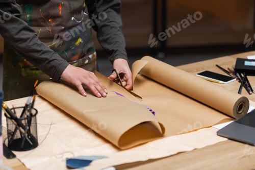 Preview: Cropped view of african american craftswoman cutting craft paper while packaging clothes in workshop