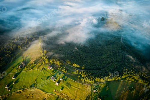 Preview: Aerial view of green valley shrouded in morning mist, with scattered farmhouses dotting landscape.