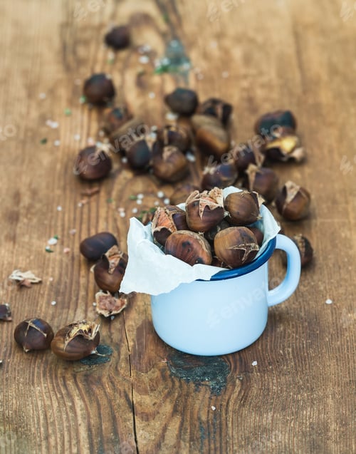 Preview: Roasted chestnuts in blue enamel mug on rustic wooden background, selective focus.
