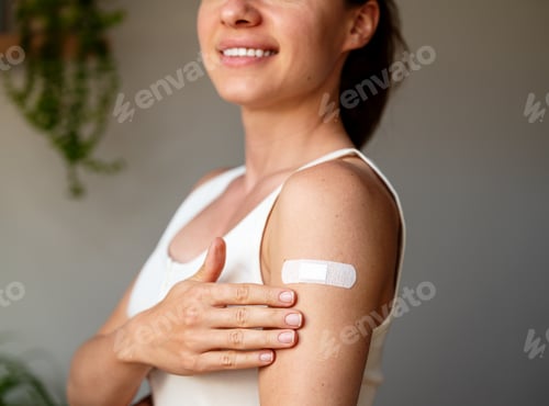 Preview: Young smiling woman showing adhesive bandage after vaccine shot