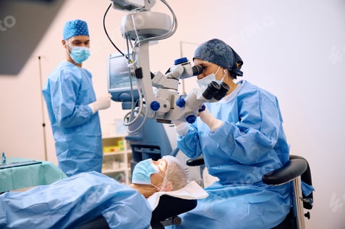 Preview: Female ophthalmologist looking through microscope during eye surgery of a patient.