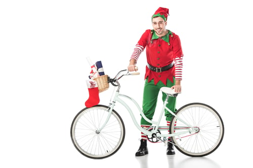 Preview: happy smiling man in christmas elf costume standing near bike with basket full of presents isolated