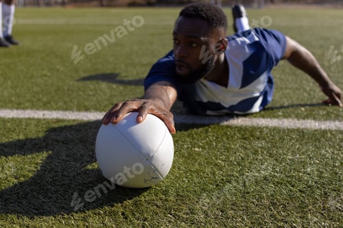 Preview: African American young male athlete reaching for a rugby ball on grass to score a try