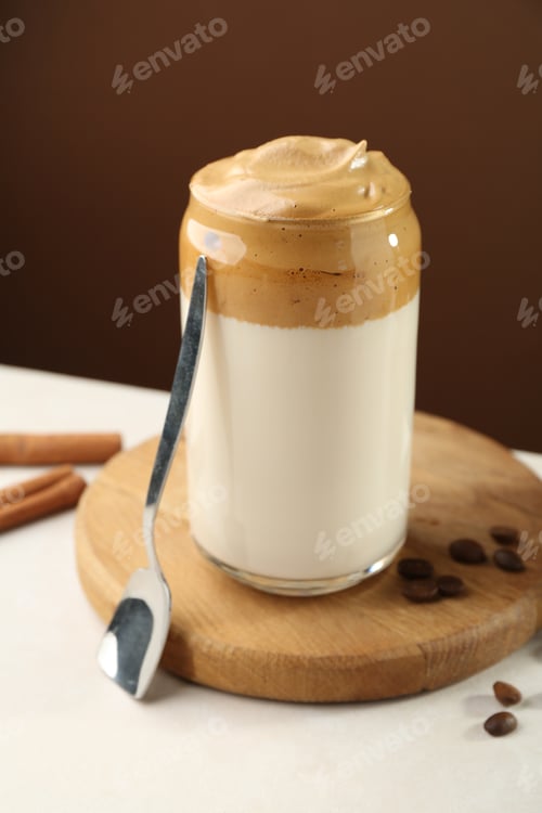 Preview: Delicious dalgona coffee in glass, beans and cinnamon on white table, closeup