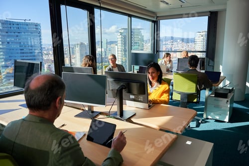 Preview: Business team working on computers in modern office with city view.