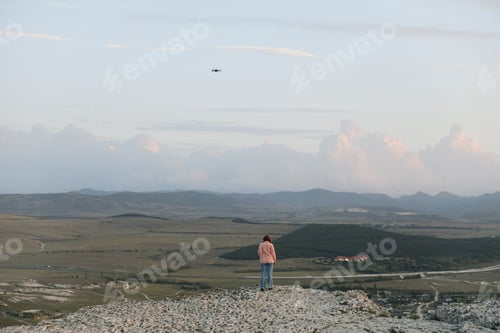 Preview: Person standing on top of hill with kite flying in the sky, enjoying a relaxing and peaceful moment