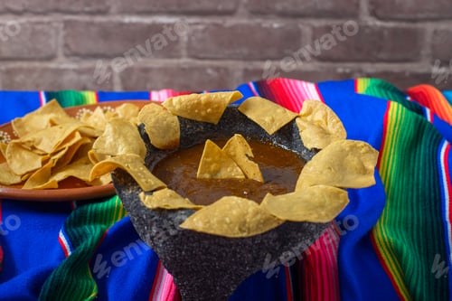 Preview: Totopos around a molcajete with red sauce on a colorful serape.
