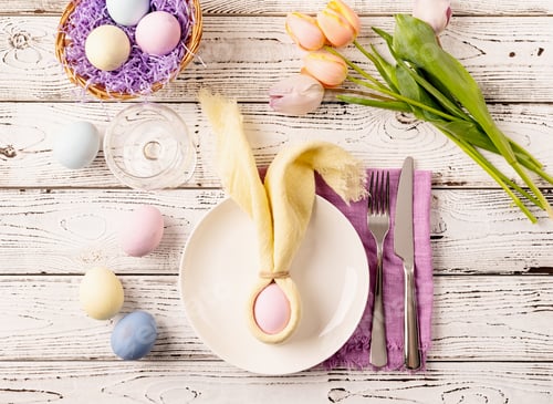 Preview: Table setting for Easter feast. Easter eggs, bunny, tulips and cutlery top view flat lay on white ru