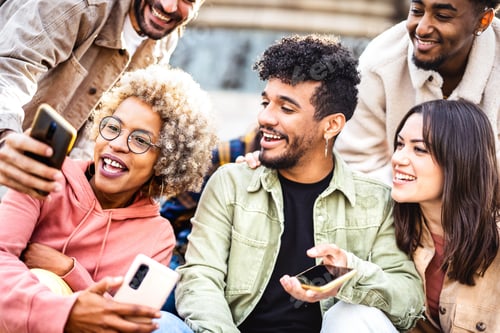 Preview: Multiracial friends having fun with mobile phone at campus college yard