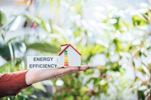 Preview: cropped view of man holding card with lettering and carton house in hands, energy efficiency at home