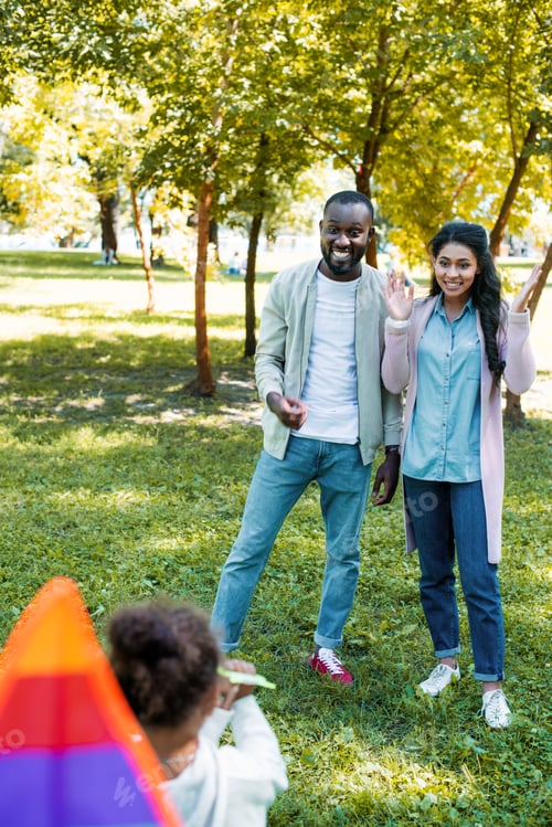 Preview: back view of african american daughter showing kite to happy parents in park