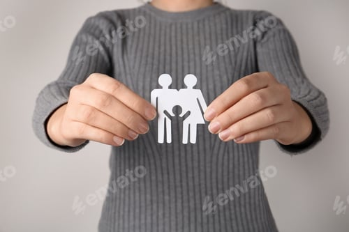 Preview: Woman holding paper silhouette of family on grey background, closeup. Life insurance concept