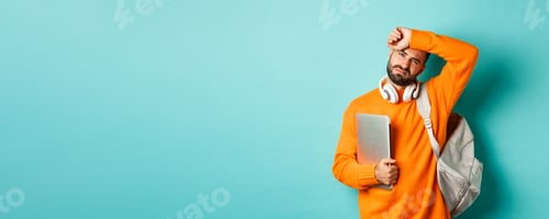 Preview: Tired male student wiping sweat off forehead, holding laptop and backpack, standing in orange