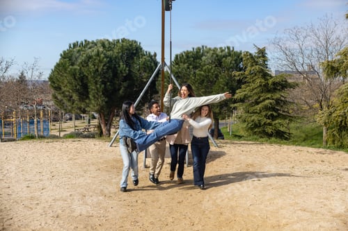 Preview: Happy friends spinning on a swing in a playground, enjoying a sunny day