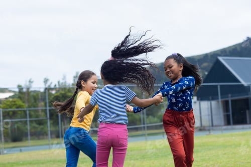 Preview: Three girls are joyfully holding hands and spinning in a grassy field in school