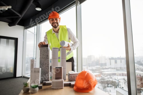 Preview: Qualified architect or engineer in reflective vest and hardhat inspecting skyscraper model