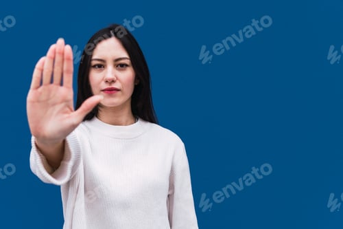 Preview: Displeased asian woman standing with hand on hip and pointing with finger while showing stop sign