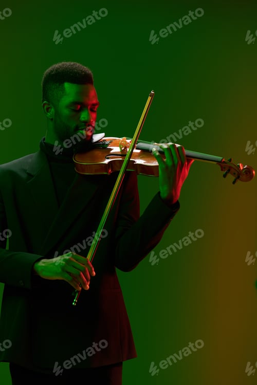 Preview: Elegant man in suit performing on violin under green and red lights on stage at night