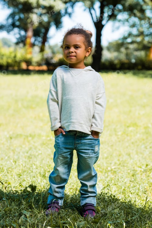 Preview: adorable african american child in jeans and sweater standing in park and looking at camera