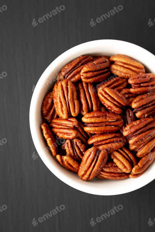 Preview: Homemade Shelled Pecans in a bowl on a black surface, top view. Flat lay, overhead, from above.