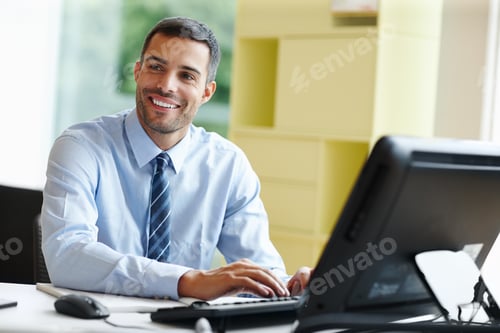 Preview: Working with a smile. A smiling young businessman sitting at his desk and working.