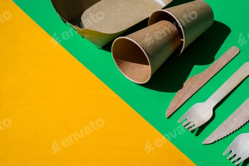 Preview: Wooden forks and paper cups with plates on color background. Eco friendly disposable tableware. Used