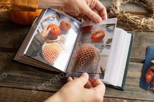 Preview: Hands put autumn printed photos in picture album.