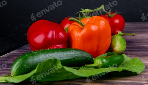 Preview: close-up view of vegetables as cucumber, pepper, tomato with leave on wooden surface and black