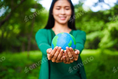 Preview: An Asian woman holds a globe in green forest,symbolizing importance preserving nature.emphasizes
