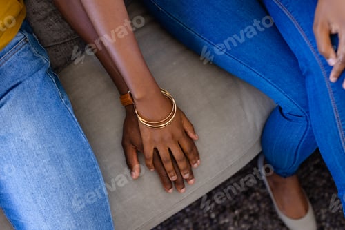 Preview: Midsection of african american couple holding hands sitting on couch at home
