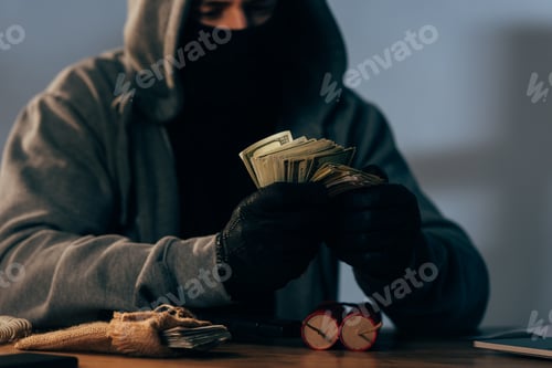 Preview: Partial view of terrorist in mask counting dollar banknotes
