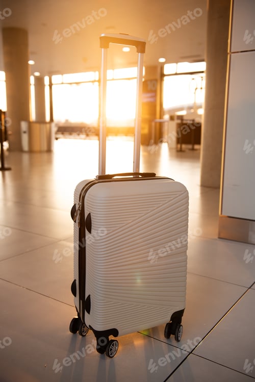 Preview: White suitcase stands in airport terminal at sunset