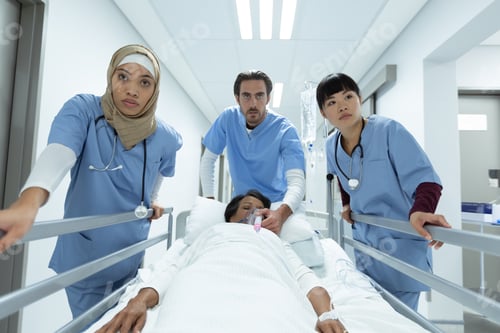 Preview: Diverse medical team pushing emergency stretcher bed in corridor at hospital.
