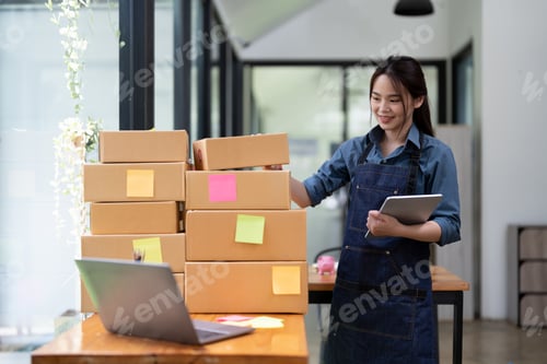 Preview: Young attractive asian woman owner startup business with box at home prepare parcel delivery in sme