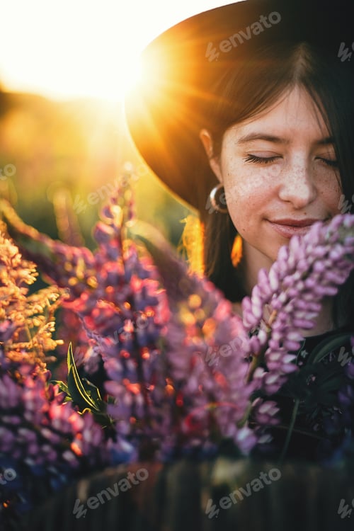 Preview: Portrait of woman with lupine bouquet in sunset light in countryside field. Atmospheric moment