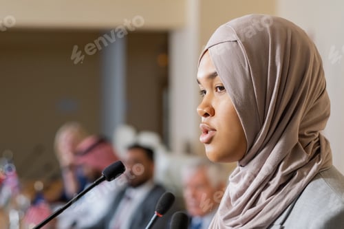Preview: Young pretty female speaker in hijab talking to audience at conference