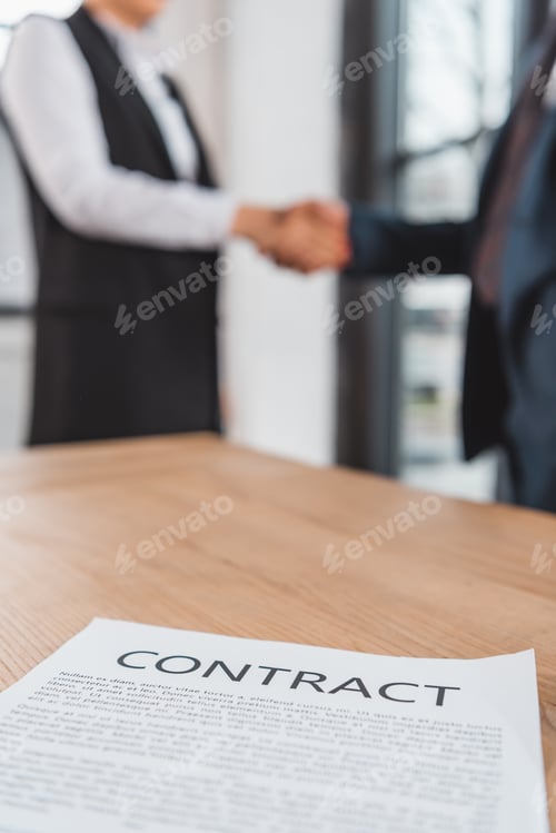 Preview: close-up view of contract on table and business people shaking hands behind