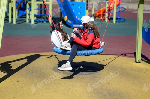 Preview: two teenager girls in caps on the playground. children's swing.