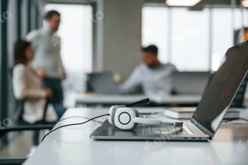 Preview: Headphones is lying down on the laptop. Men and woman are working in the office together