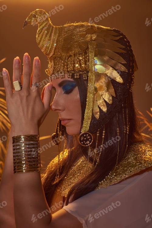Preview: Woman in egyptian costume doing praying hands gesture near blurred plants on brown background