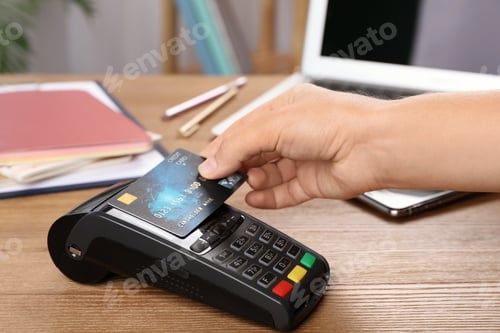 Preview: Woman using terminal for contactless payment with credit card at table