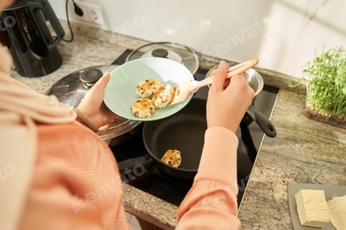 Preview: Cropped photo of young woman cooking cheese pancakes with raisins in kitchen