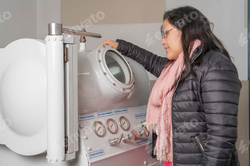 Preview: Woman standing looking at a hyperbaric treatment machine.